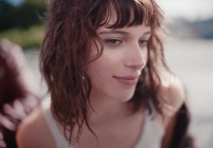 A carefree young woman with wavy brown hair smiles as it blows in the wind in slow motion