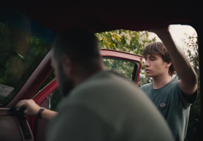 A father and son share a quiet moment cleaning the interior of their old red pickup truck together
