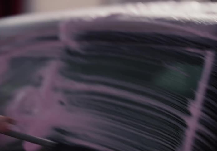 Slow motion close-up of a smiling young woman scrubbing her car with pink soap and a brush at a car wash