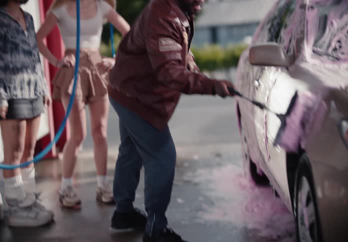 A diverse group of young friends laugh and have fun together while washing a car with pink soap at an outdoor car wash