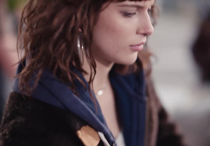 A close-up, slow-motion profile of a pensive young woman with brown wavy hair looking down thoughtfully
