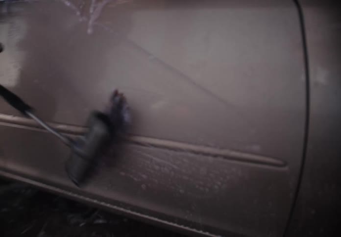 A happy young woman scrubs her car with a soapy brush and rinses it off at a self-service car wash