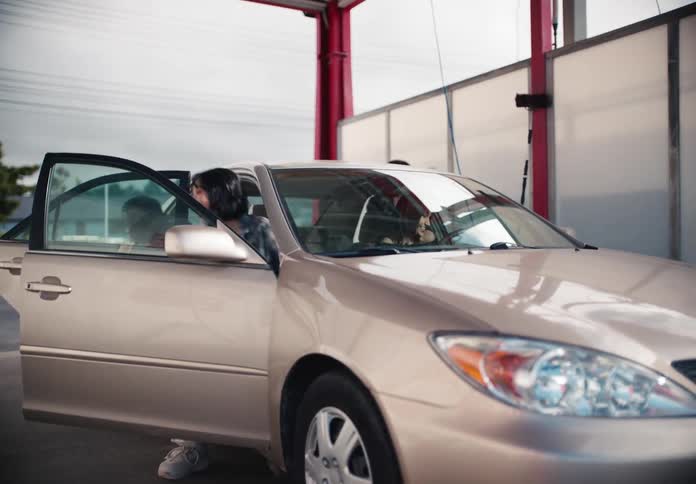 A gold sedan pulls into a car wash bay, and two smiling young women get out to begin washing it