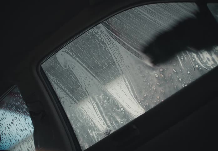 Interior shot of a car window being scrubbed with soap and a brush at a self-service car wash