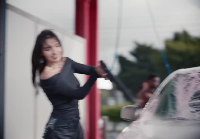 A stylish young woman joyfully washes her car with pink foam at a self-service car wash bay in slow motion
