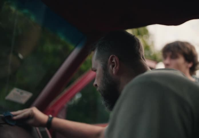 A man with a beard carefully details the dashboard of his classic red car with a blue cloth
