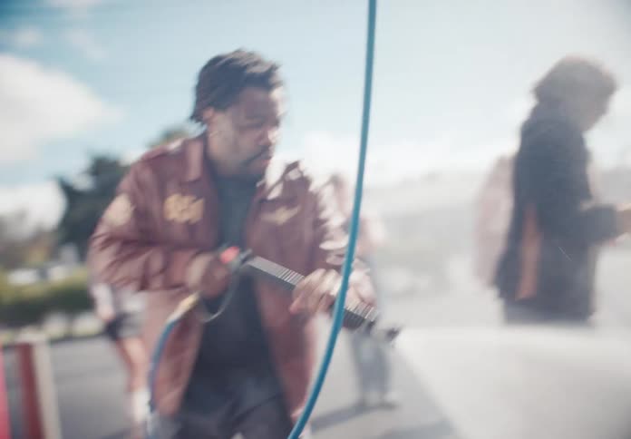 A man in a leather jacket energetically pressure washes a car at a self-service car wash on a bright, hazy day