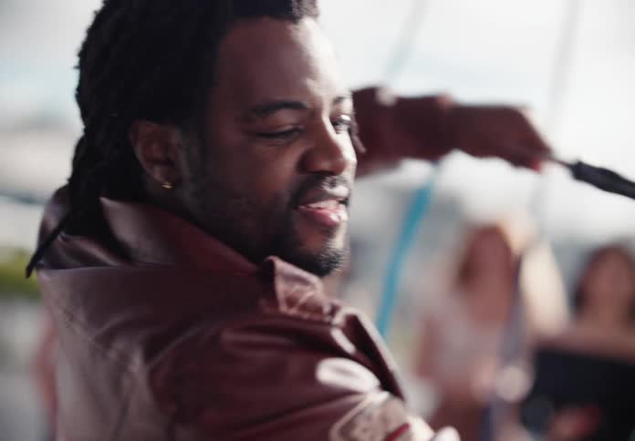 A happy man with dreadlocks smiles and dances while washing a car with a large brush and pink soap in slow motion