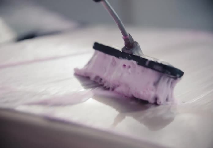 Close up slow motion of a person scrubbing the hood of a silver car with a soapy pink brush