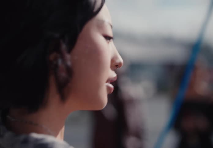 A close-up, slow-motion shot of a young Asian woman's profile as the wind blows through her hair outdoors