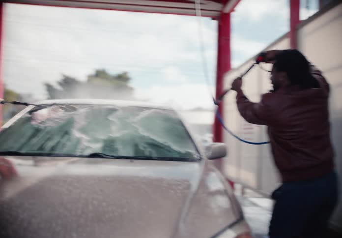 A group of friends have fun together while washing their car with a pressure washer and a brush at a self-service car wash in slow motion