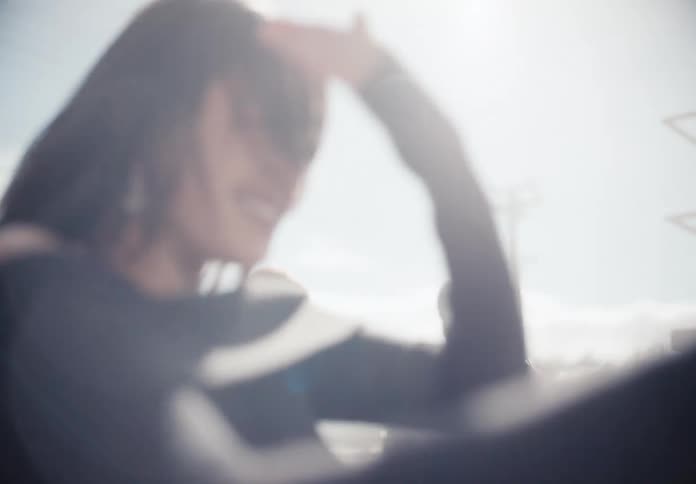 Slow motion shot of a joyful young woman laughing as she gets sprayed with water while washing her car on a sunny day
