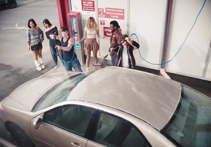 High angle view of a diverse group of cool friends laughing and having fun while washing a car at a self-serve car wash