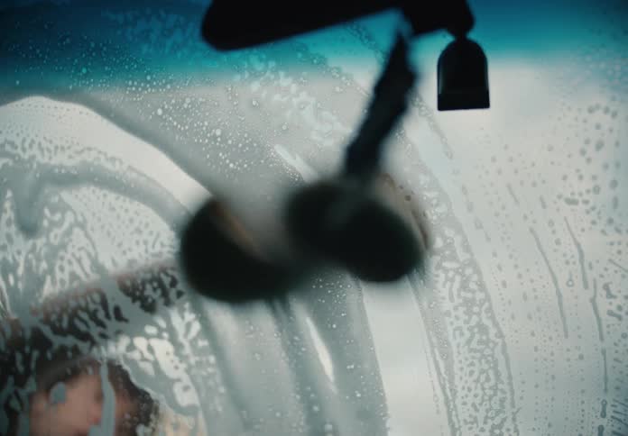 Slow motion shot from inside a car of a person washing the soapy windshield with a sponge