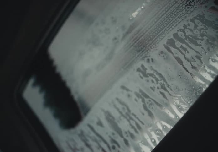 Soapy brushes scrub a car's sunroof clean in an automatic car wash, viewed from inside