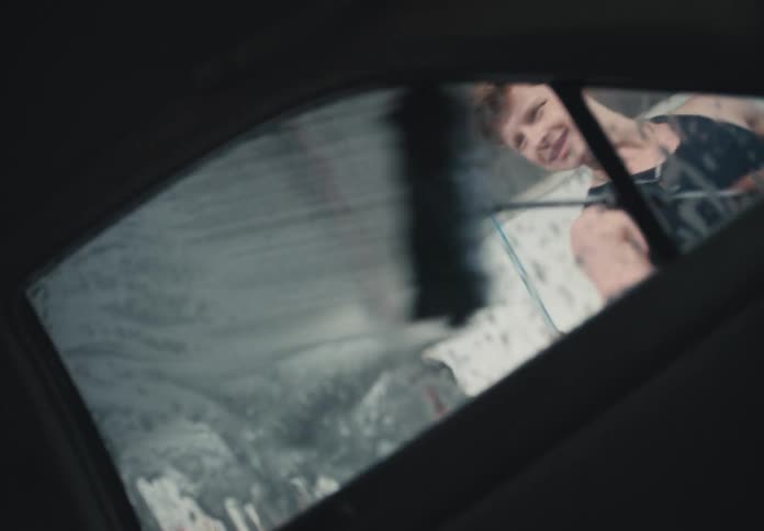 View from inside a car as a smiling young man scrubs the sudsy rear window at a self-service car wash