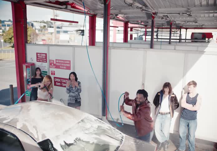 A diverse group of young friends hang out and wash their car together at a self-service car wash