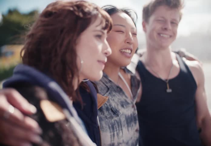 Carefree and happy young friends smile and laugh together as they walk arm in arm outside in slow motion