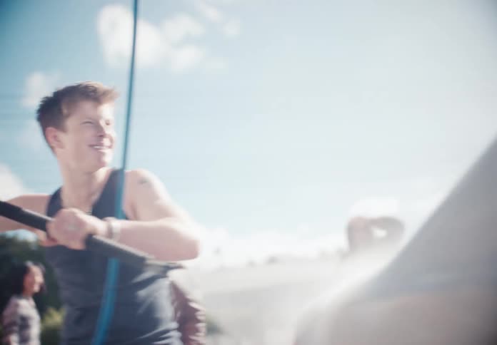 Happy friends playfully fight over a pressure washer while washing a car at a self-service car wash on a sunny day