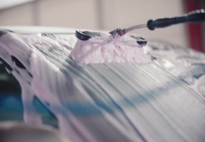 A soapy brush with pink foam cleans a car's windshield and hood in slow motion at a self-service car wash