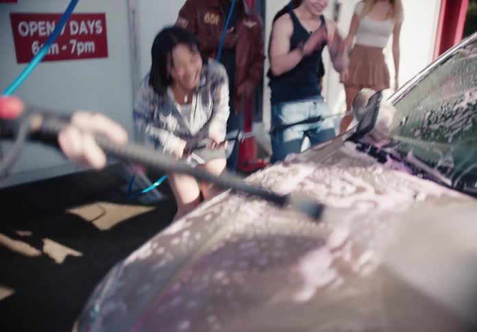 A diverse group of happy young friends laugh and have fun together while washing a car at a self-service wash in slow motion
