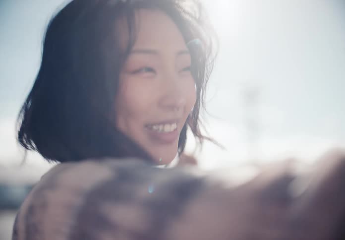 A slow-motion close-up of a joyful young Asian woman smiling and laughing in the bright sunshine, her hair blowing in the wind