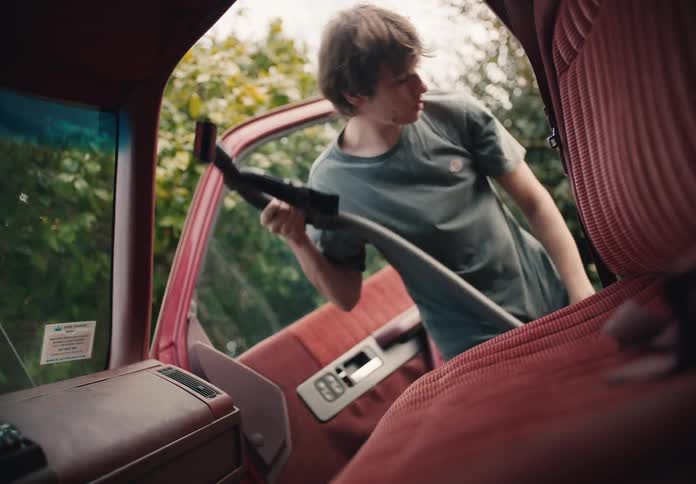 Interior view of a young man vacuuming the red fabric seats and floor of an old truck