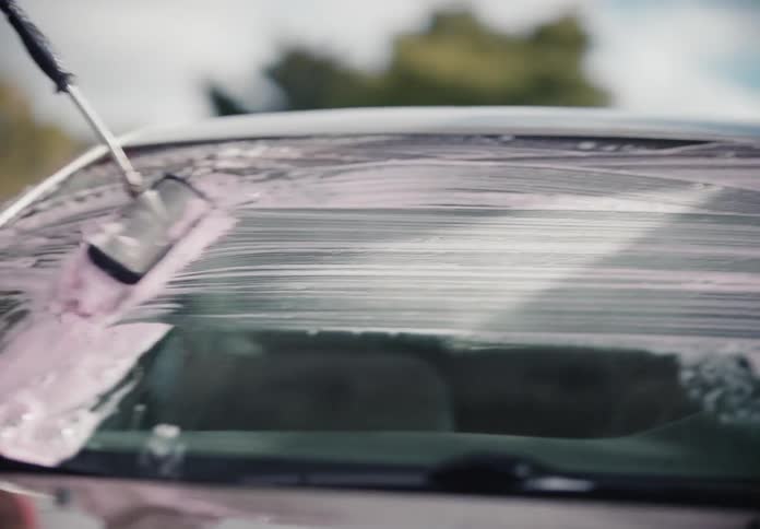 A young man scrubs the windshield of a car with a soapy brush at a self-service car wash