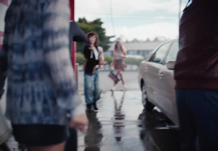 A stylish group of diverse friends have fun washing their car together in slow motion at a self-service car wash