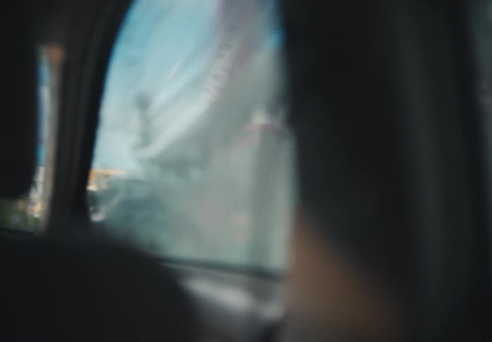 Friends wash a car together at a self-service car wash, seen through the soapy back window