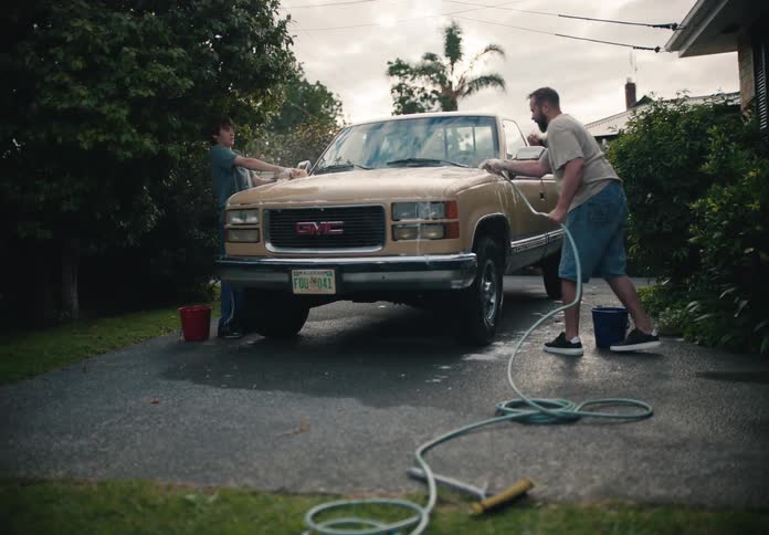 A father and son bond while washing a classic GMC pickup truck together in the driveway of their home