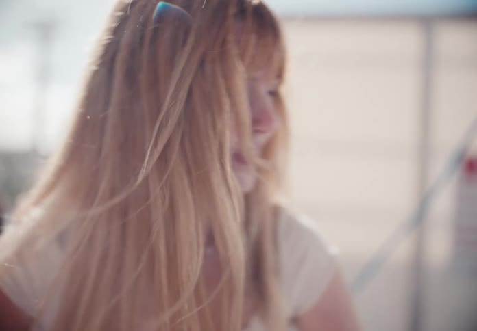 Slow-motion close-up of a stylish young woman with blonde hair using a pressure washer at a car wash on a sunny day