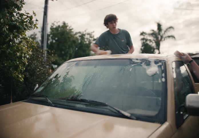 A father and his teenage son wash their vintage pickup truck together in the driveway in slow motion