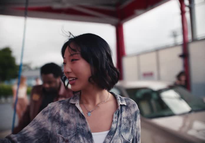 A group of diverse friends get out of their car at a self-service car wash, and an Asian woman walks toward the payment machine in slow motion