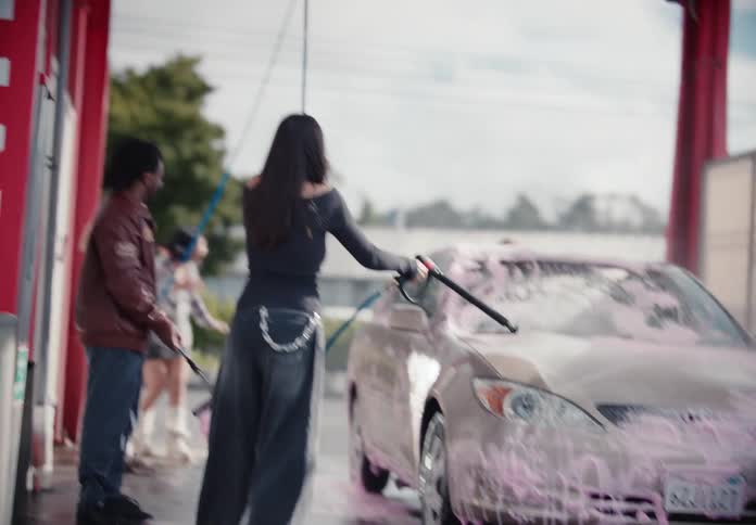A stylish group of young friends have a fun time washing a car with pink soap at a self-service carwash