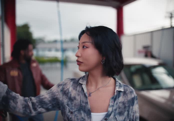 A group of friends gets out of a car at a self-service wash, and a woman walks towards the controls in slow motion