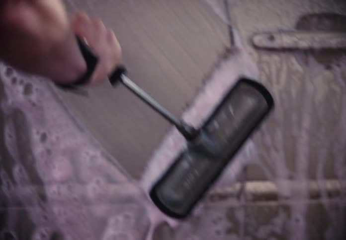 A person scrubs the side of their car with a foamy pink soap brush at a self-service car wash in slow motion