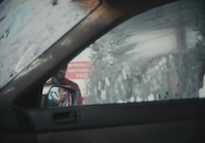 A view from inside a car as friends work together to scrub the soapy windshield and windows at a car wash