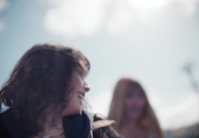 A carefree young woman with a nose ring and wavy hair smiles and laughs joyfully in the sunlight in slow motion