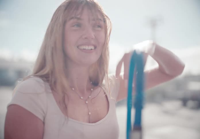 A happy couple has a playful water fight at a car wash on a bright sunny day in slow motion