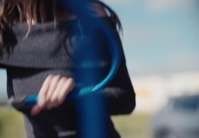 A joyful young woman laughs and smiles in slow motion while holding a pressure washer at a car wash on a sunny day