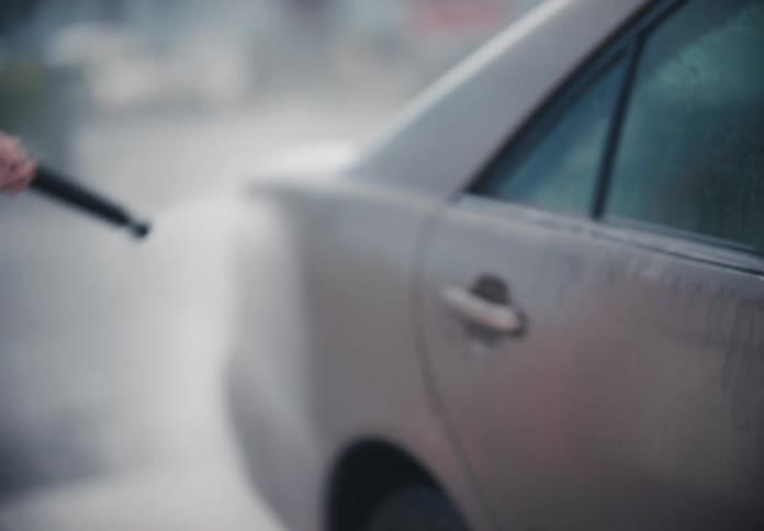 Slow motion close-up of a woman using a pressure washer to clean her car at an outdoor car wash