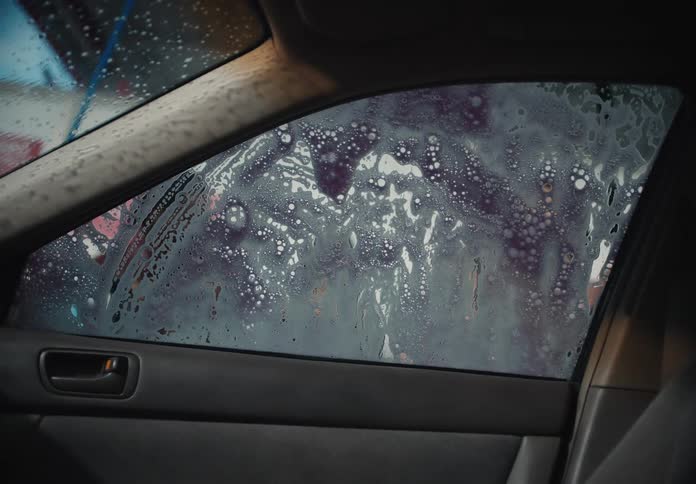 View from inside a vehicle as a window is scrubbed with purple soap at a car wash