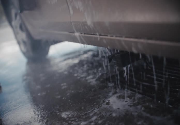 Low-angle close-up of a car being washed, with soapy water dripping onto the wet floor in slow motion