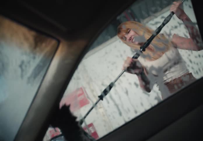 Interior car view of a young woman happily washing the vehicle's windshield with soap and a brush at a self-service car wash