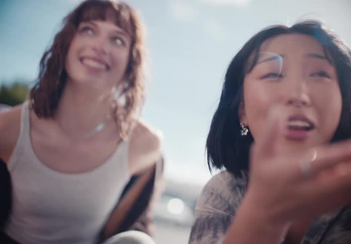 A cinematic, low-angle slow-motion shot of two diverse young women laughing and talking together on a sunny day