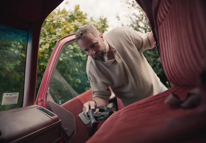 A man opens the door of his vintage red truck and meticulously vacuums the interior seats and door panels