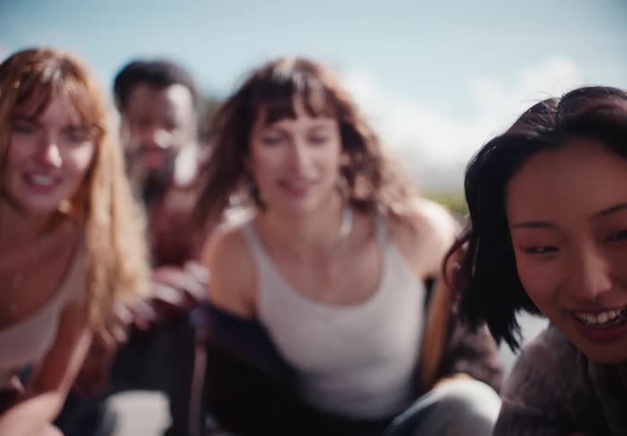 A young woman's pensive mood lifts into a smile while riding with her diverse group of friends in the back of a truck in slow motion