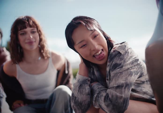 A diverse group of happy friends laugh and hang out together outdoors on a sunny day in slow motion