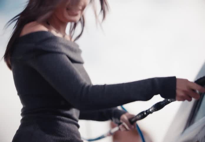 A stylish young woman washes a car with a pressure washer at a self-service car wash in slow motion